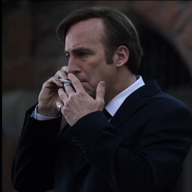 a man in a suit talking on a cell phone while holding his hand to his mouth