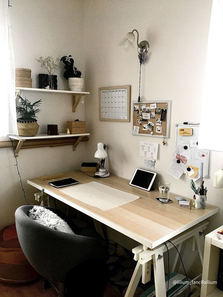 a desk with a laptop on top of it in front of a window next to a chair