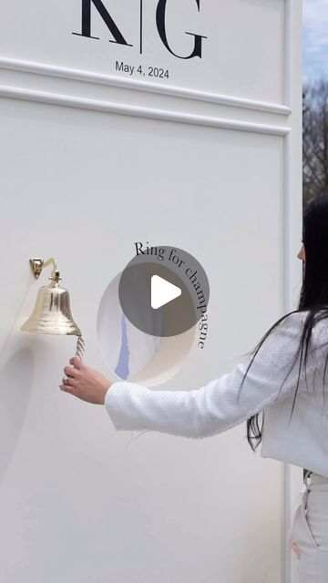 a woman holding a bell in front of a white wall with the words king and queen on it