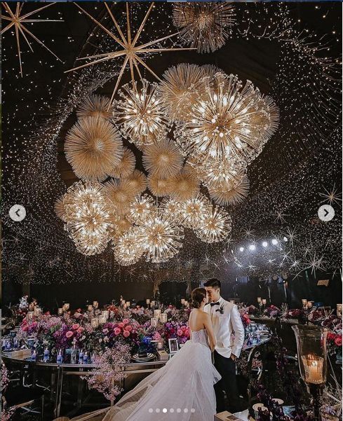 a bride and groom standing under a chandelier in front of a large crowd