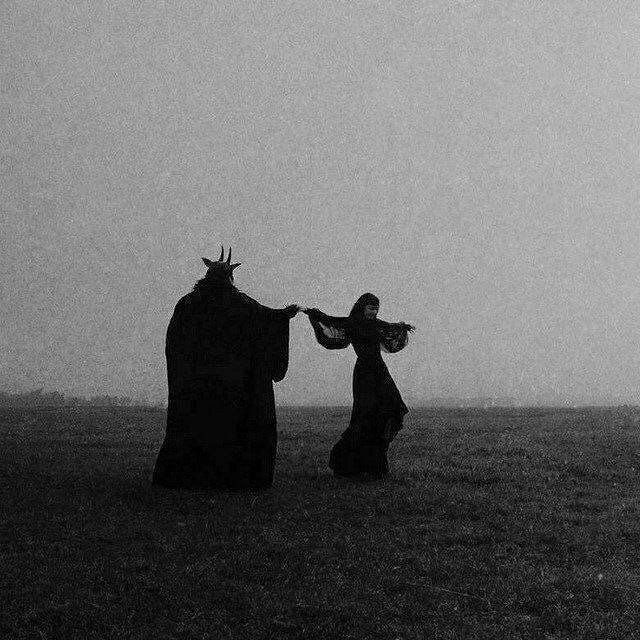 black and white photograph of two people dressed as witches standing in a field, facing each other