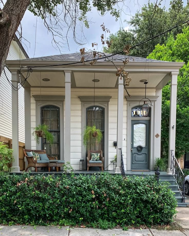 a white house with two front porches and some bushes on the side of it