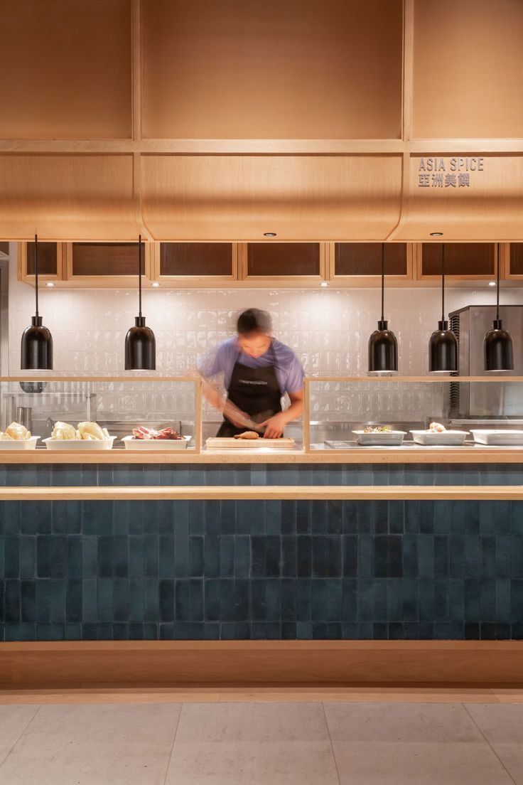 a man standing behind a counter in a kitchen with blue tiles on the floor and wooden cabinets