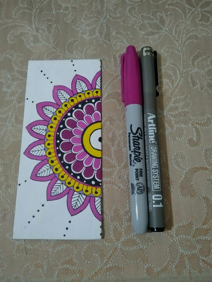 a pink pen sitting next to a notepad with a flower design on the cover