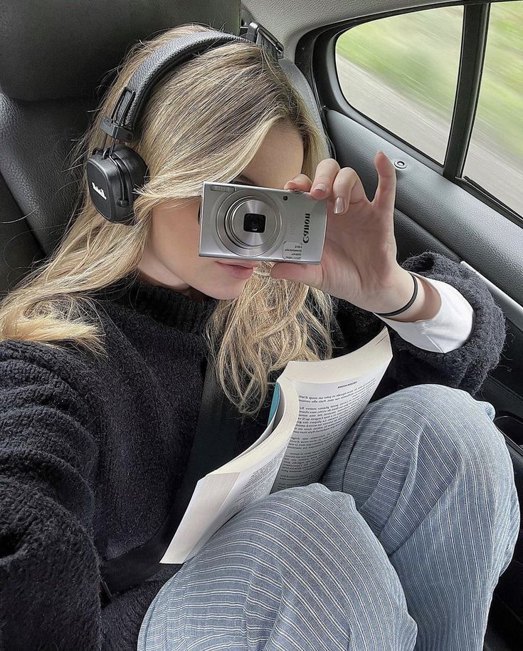 a woman sitting in the back seat of a car with headphones on and reading a book