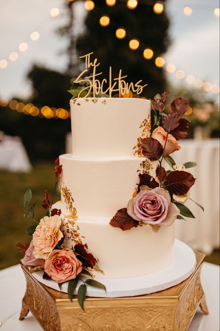 a three tiered cake with flowers and the word stockton on top is sitting on a gold stand