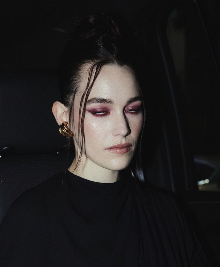 a woman sitting in the back seat of a car with her eyes closed and dark makeup