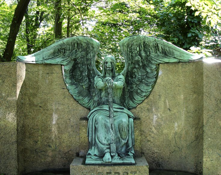 an angel statue sitting on top of a stone slab in the middle of a forest