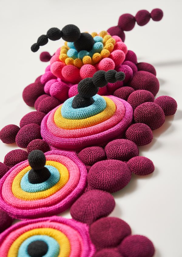 several knitted objects are lined up on a table top, one is multicolored and the other is black