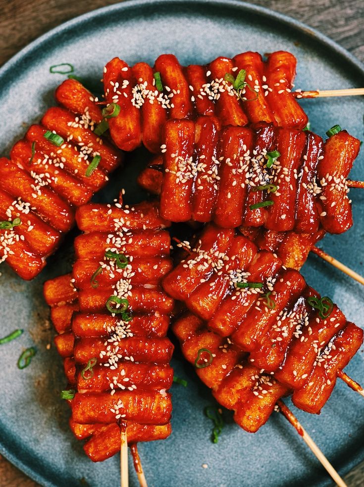 several skewered meats with sesame seeds and seasoning on a blue plate