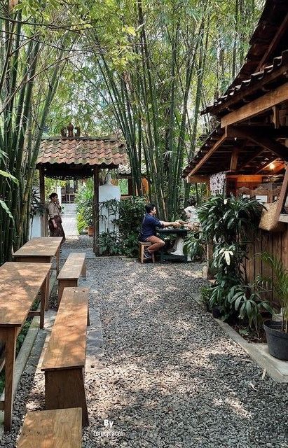 two people sitting on benches in the middle of a garden with lots of trees and plants