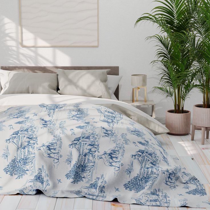 a bed with blue and white linens in a room next to potted plants