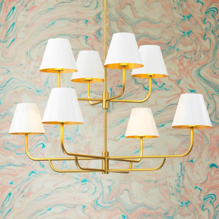 a gold chandelier with white lamps hanging from it's sides in front of a marble wall