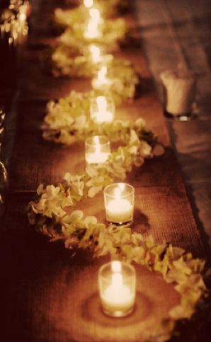 a long table with candles and flowers on the runner line, along with tea lights