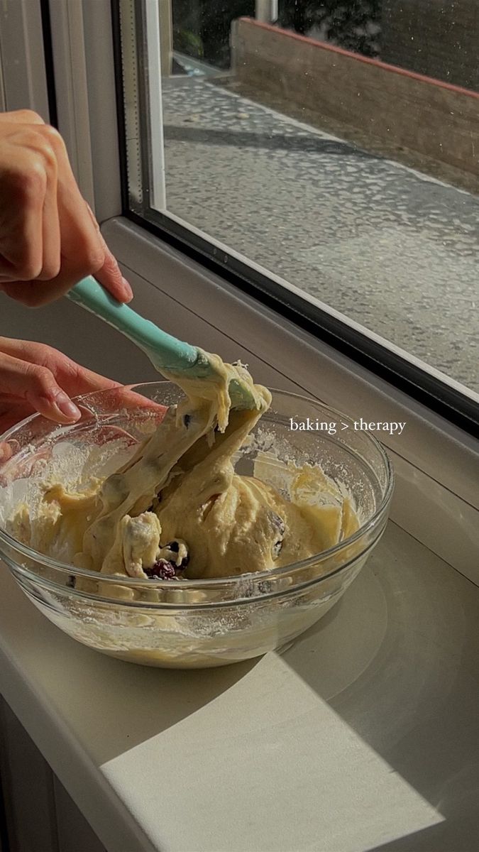 someone is mixing batter in a bowl on the window sill with a green spoon