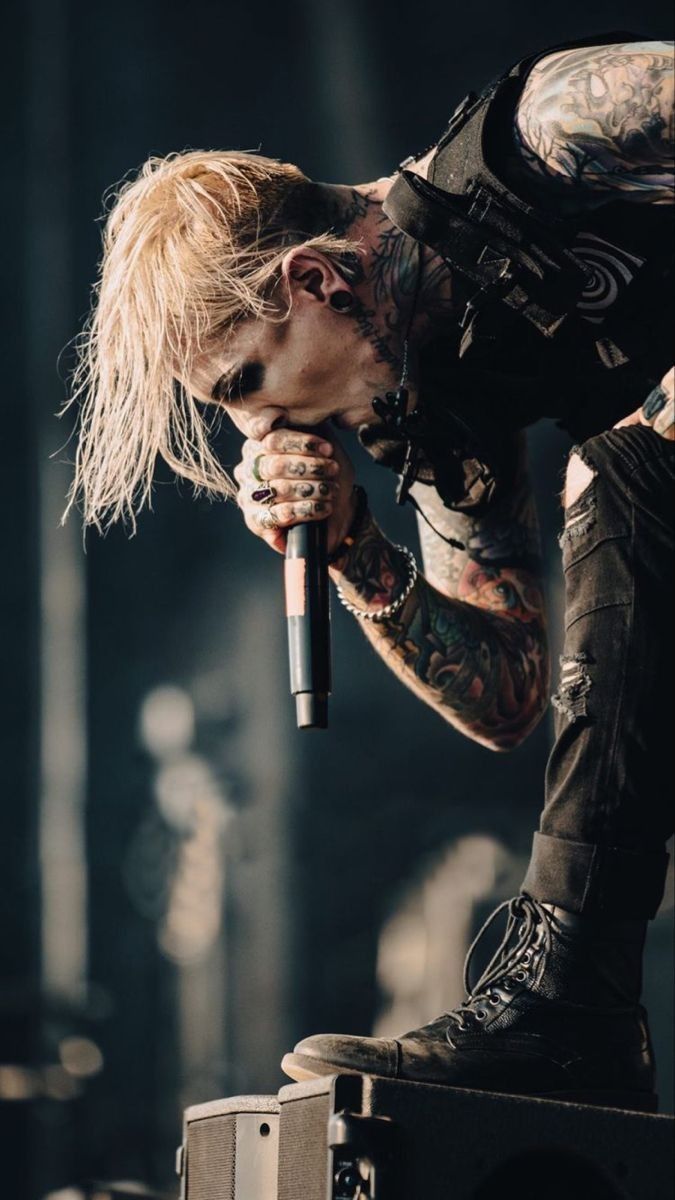 a man with tattoos holding a microphone on top of his head and looking down at the ground