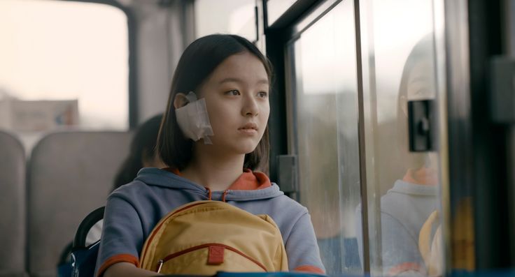 a woman sitting on a bus with her back to the camera and wearing ear buds