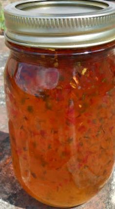 a jar filled with lots of food sitting on top of a stone floor next to grass