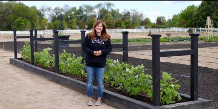 a woman standing in front of a row of raised garden beds with plants growing on them