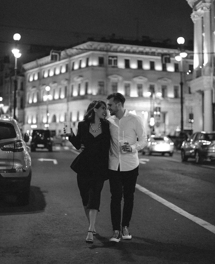 a man and woman walking down the street in front of a large building at night