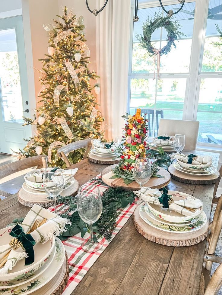 a dining room table set for christmas with plates and place settings on the wooden table