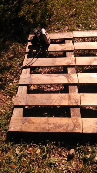 a wooden pallet sitting in the grass with a power drill on top of it