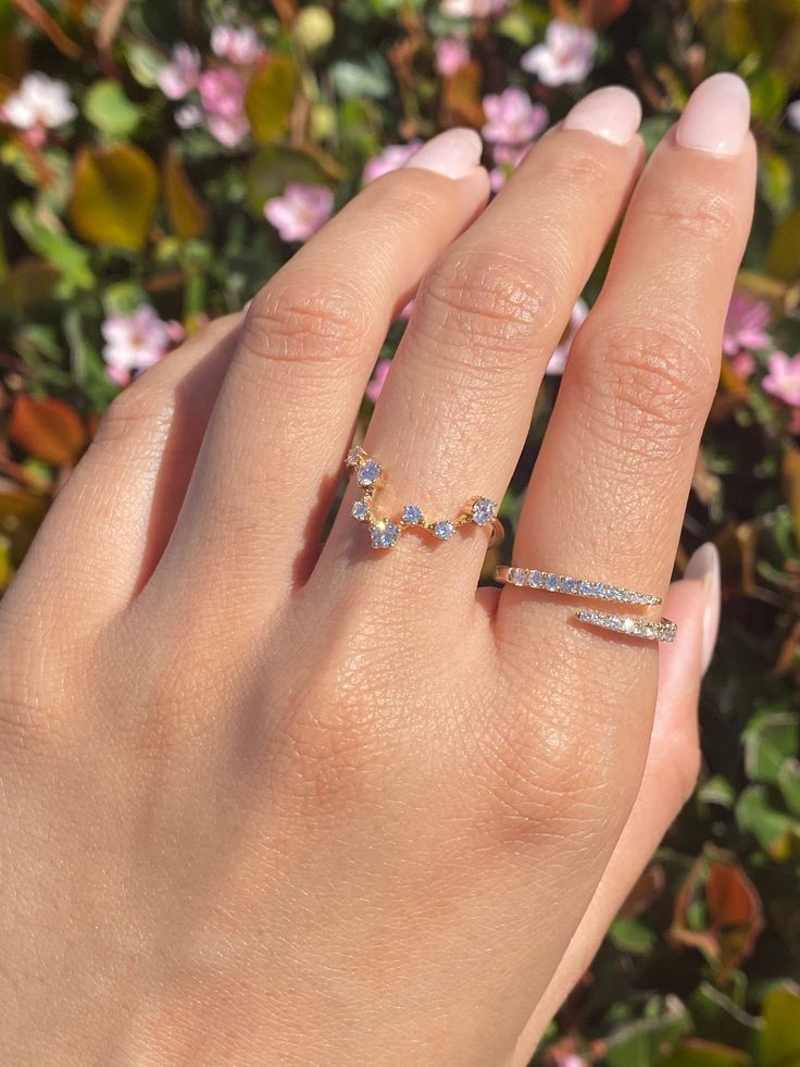 a woman's hand with two rings on it and pink flowers in the background