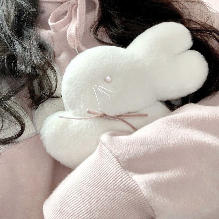 a white stuffed animal laying on top of a woman's pink shirt and sweater