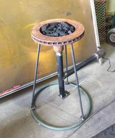 a metal stool with coal in it sitting next to a wall