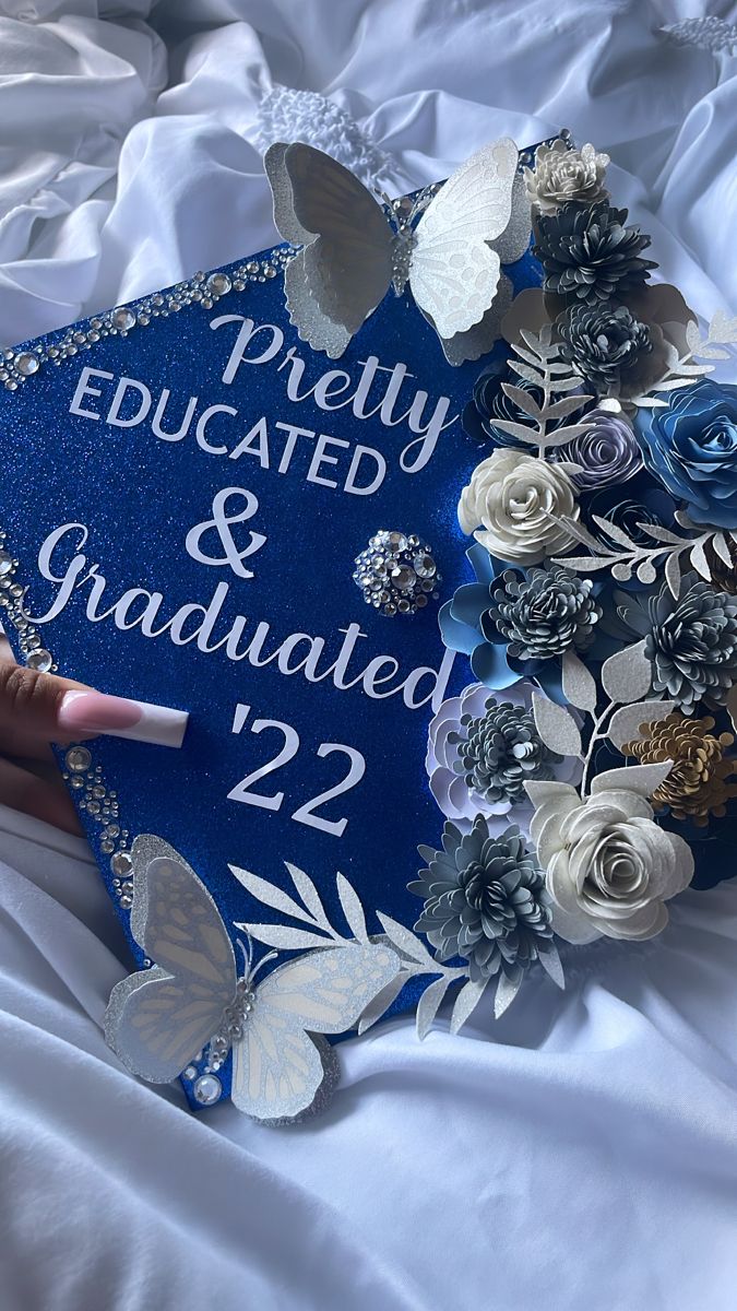 a blue graduation cap with white flowers and butterflies on it that reads pretty, dedicated & graduated 22