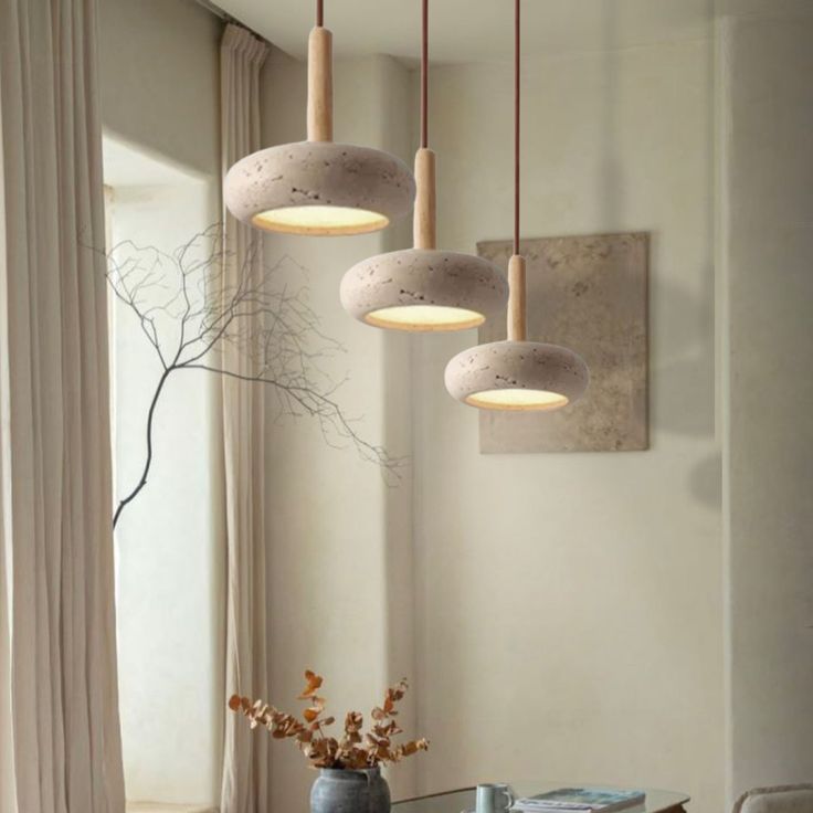 a dining room table with four lights hanging from it's ceiling and two vases filled with flowers