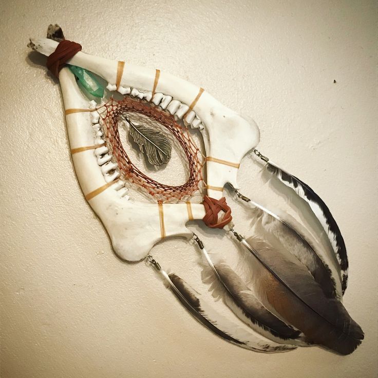 a wall hanging made out of metal and feathers on a white wall with a green arrow in the center