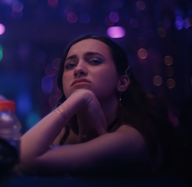 a woman sitting at a table with her hand on her chin and looking off into the distance