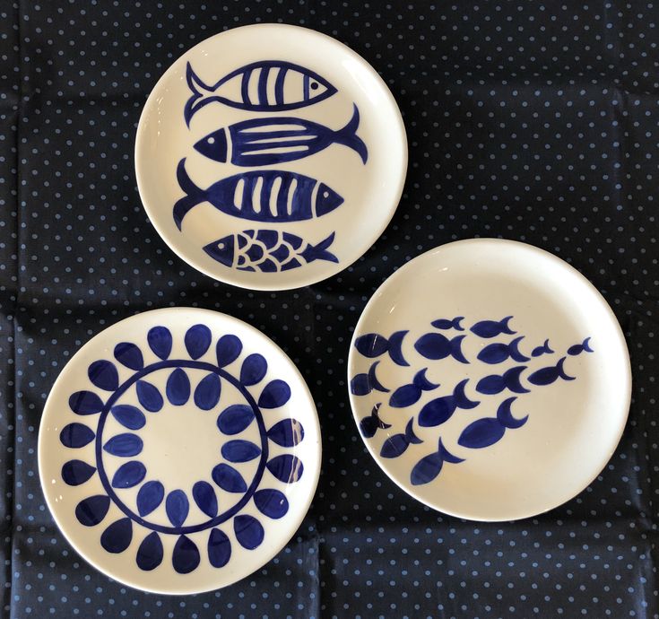 three blue and white plates with fish painted on them, sitting on a polka dot tablecloth