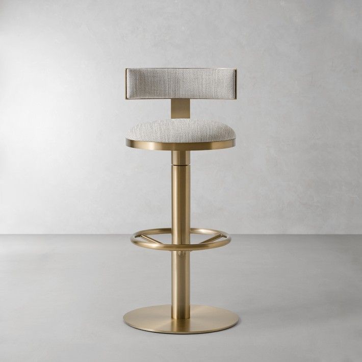 a gold stool with a white upholstered seat and back rests in front of a plain wall