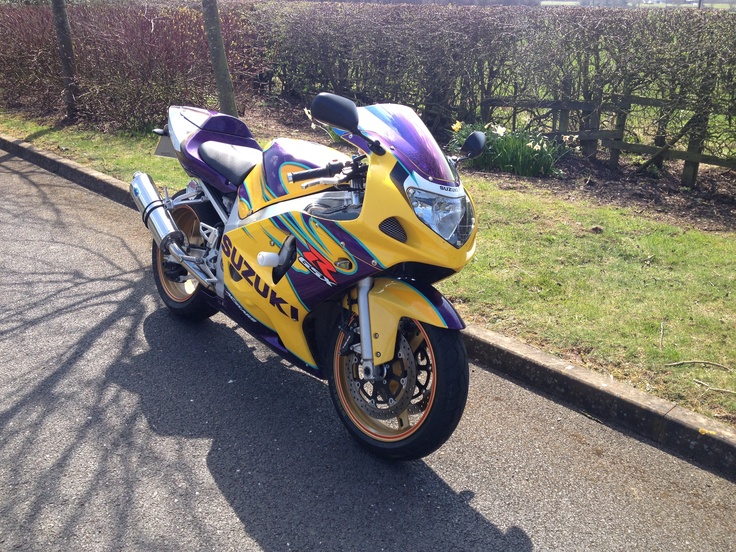 a yellow and purple motorcycle parked on the side of the road next to some bushes