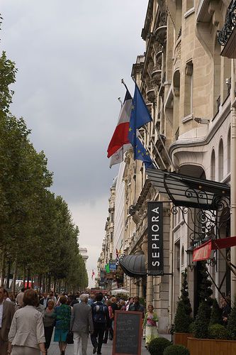 people walking down the street in front of buildings with flags hanging from it's sides