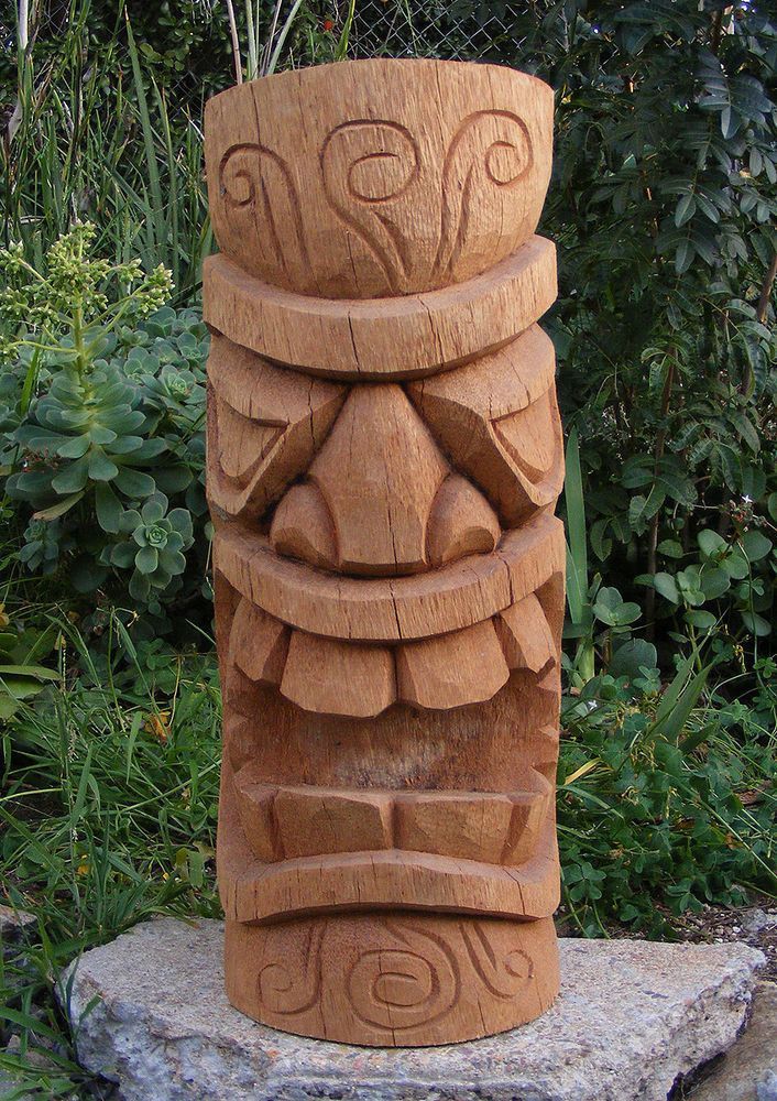 a wooden sculpture sitting on top of a stone slab in front of some bushes and trees