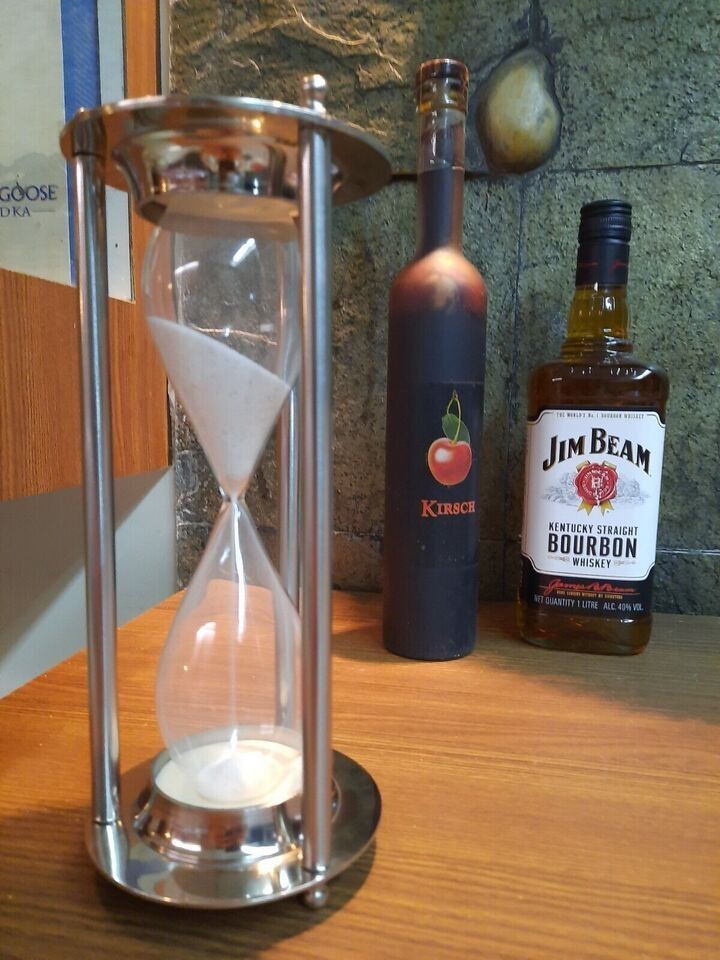 an hourglass sitting on top of a wooden table next to a bottle of rum