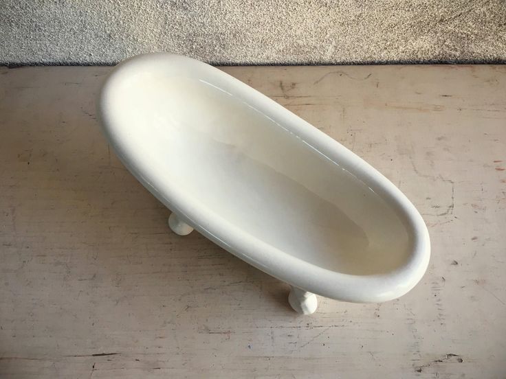 a white bathtub sitting on top of a wooden table next to a wall and cement floor