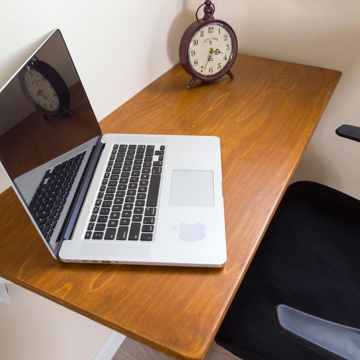 an open laptop computer sitting on top of a wooden desk next to a clock and chair