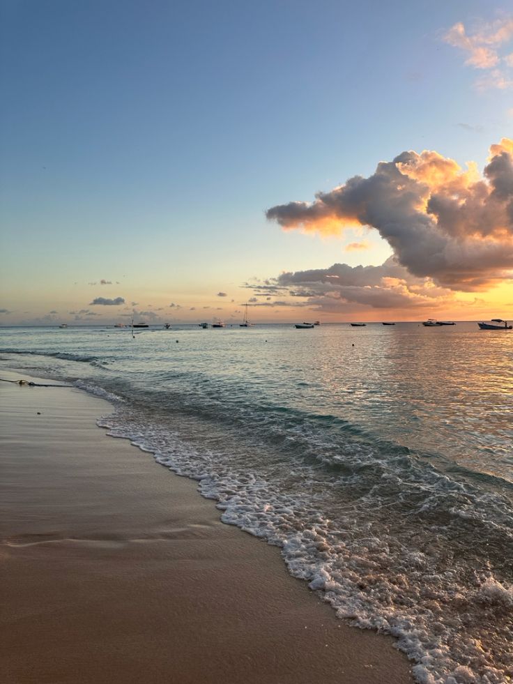 the sun is setting over the ocean and boats are in the water on the beach