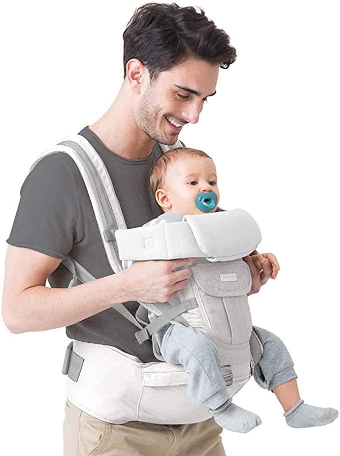 a man is holding a baby in a grey sling with a blue pacifier attached to it