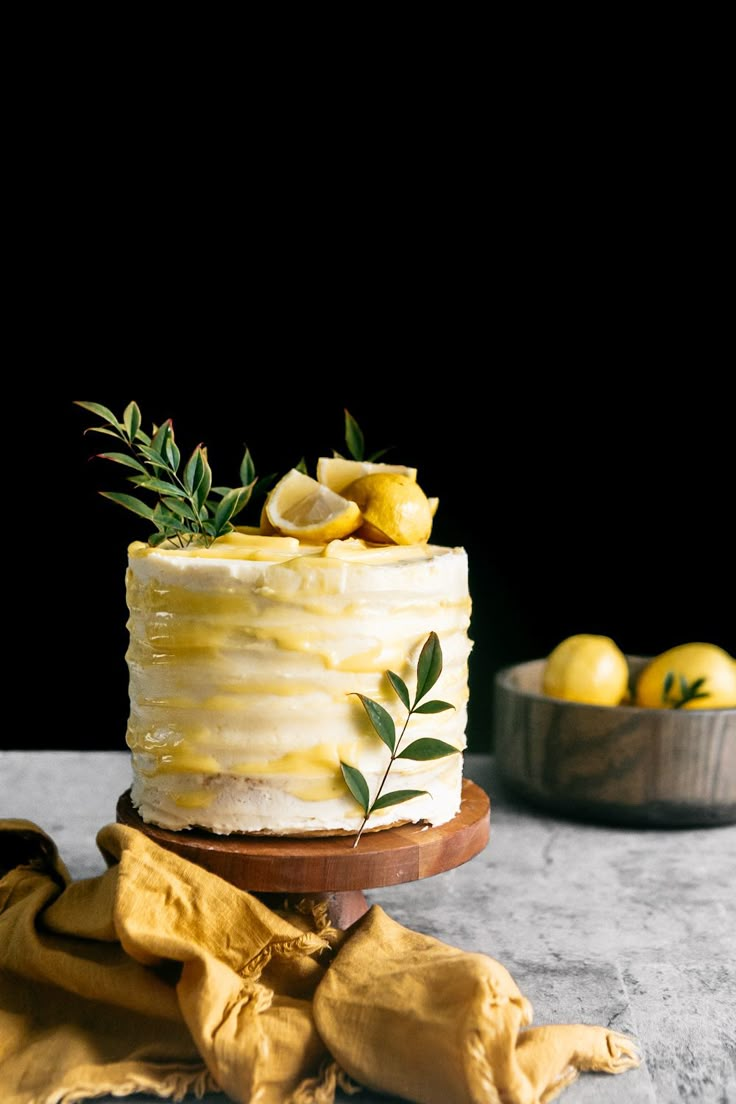 a white cake with lemons on top sitting on a wooden platter next to some yellow napkins