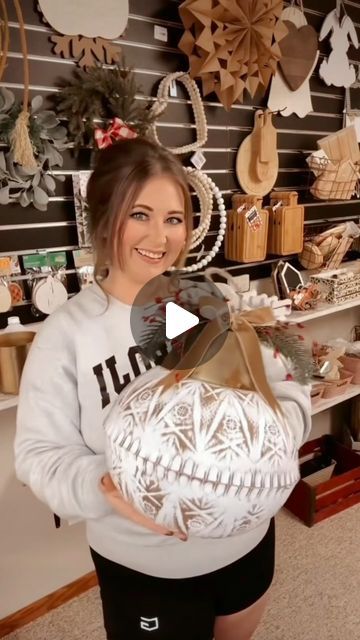 a woman holding a large white ball in front of a wall full of christmas decorations