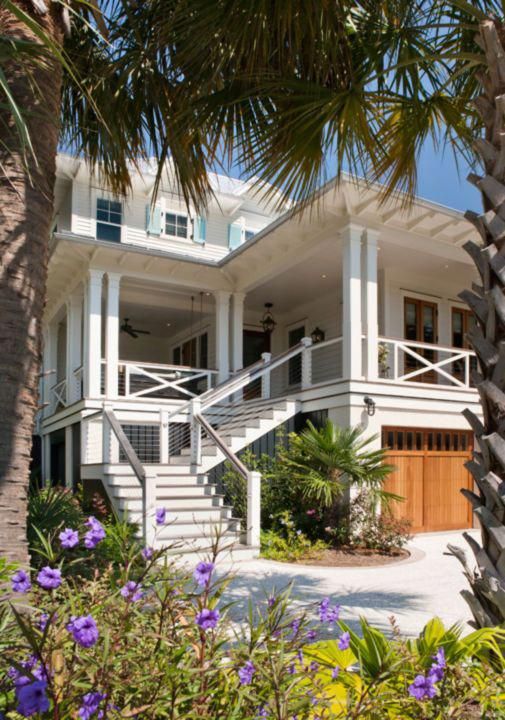 a white house surrounded by palm trees and purple flowers in the foreground with stairs leading up to it