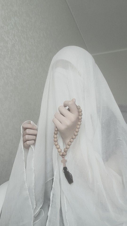 a woman wearing a white veil and holding a beaded necklace in her hand with both hands