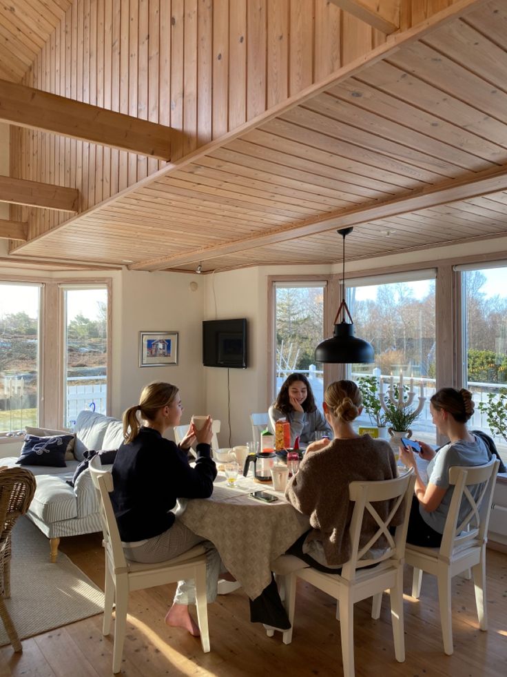 four women sitting at a table in a room with wood paneled walls and windows