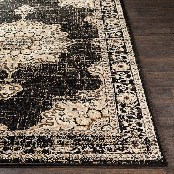 a black and beige area rug with an ornate design on the bottom, along with a wooden floor