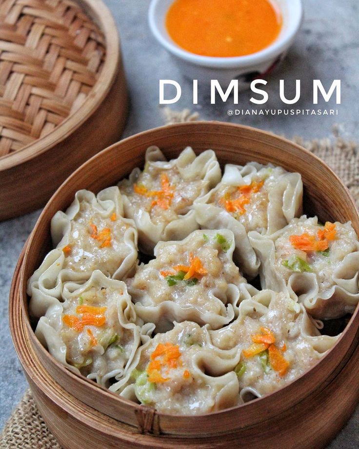 dumplings with carrots and broccoli in a wooden bowl next to dipping sauce